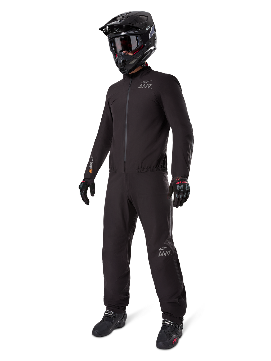 Alpinestars AMT-8 Stretch Drystar® XF Liner, fato de motociclismo impermeável preto, usado com capacete preto, óculos e luvas, com logótipos AMT e Drystar XF, equipamento de aventura funcional para proteção em todas as condições climatéricas.