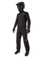 Alpinestars AMT-8 Stretch Drystar® XF Liner, fato de motociclismo impermeável preto, usado com capacete preto, óculos e luvas, com logótipos AMT e Drystar XF, equipamento de aventura funcional para proteção em todas as condições climatéricas.