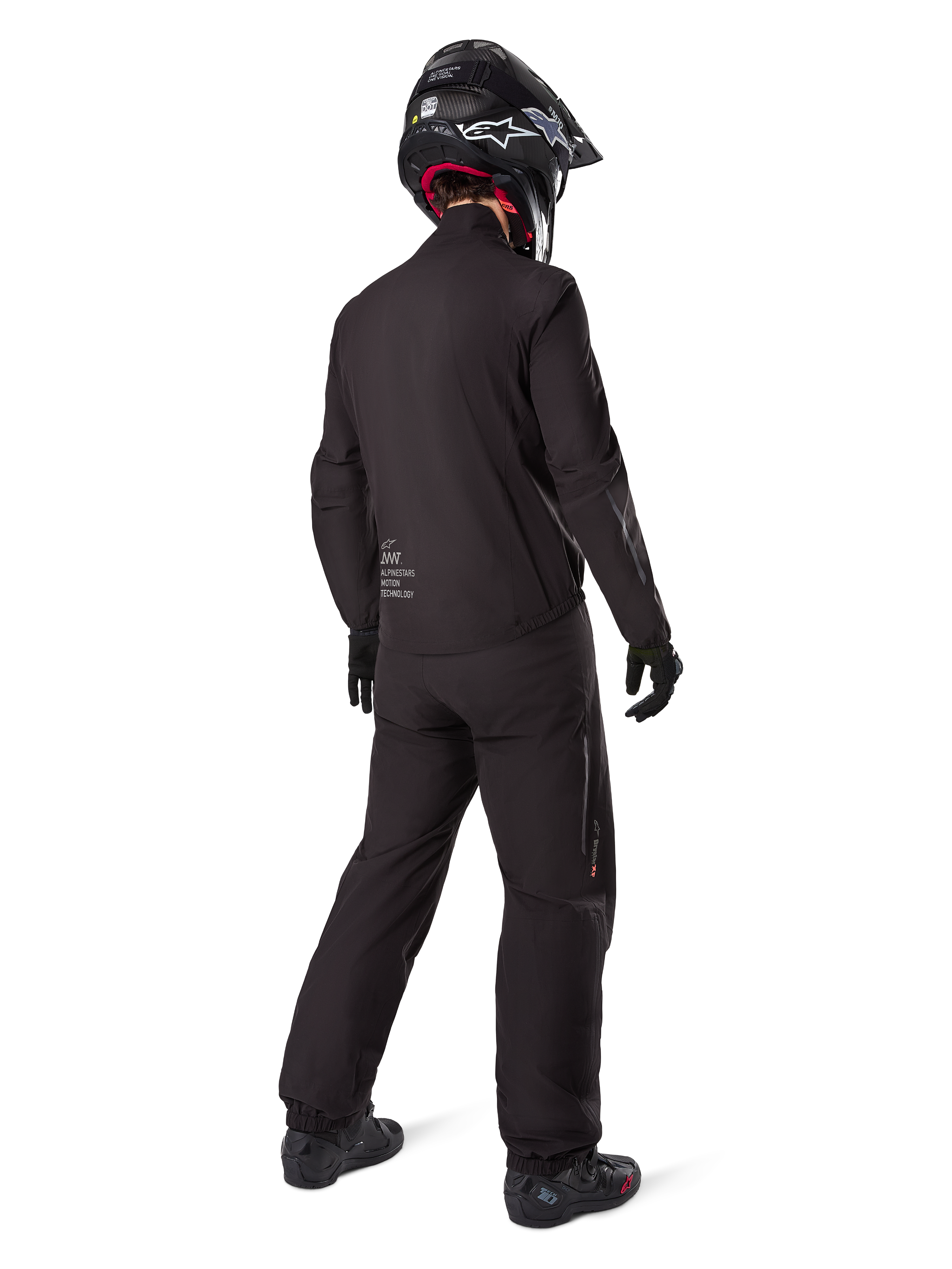 Vista traseira de um motociclista com o forro do casaco Alpinestars AMT-8 Stretch Drystar® XF, equipamento técnico de motociclismo preto, calças a condizer e capacete preto, marca "AMT Alpinestars Motion Technology" nas costas, design minimalista para adventure touring