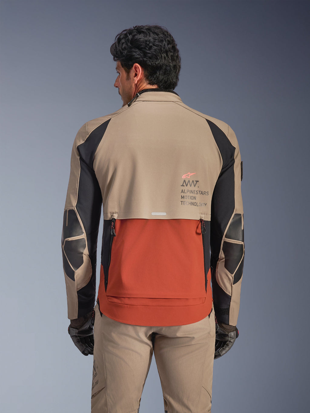Casaco Alpinestars AMT-8 Stretch Drystar® XF, Walnut Rust Black, vista traseira no modelo, realça o design de telha do escape traseiro em cor ferrugem, secções superiores em castanho nogueira, detalhes pretos nas mangas e logótipo Alpinestars Motion Technology