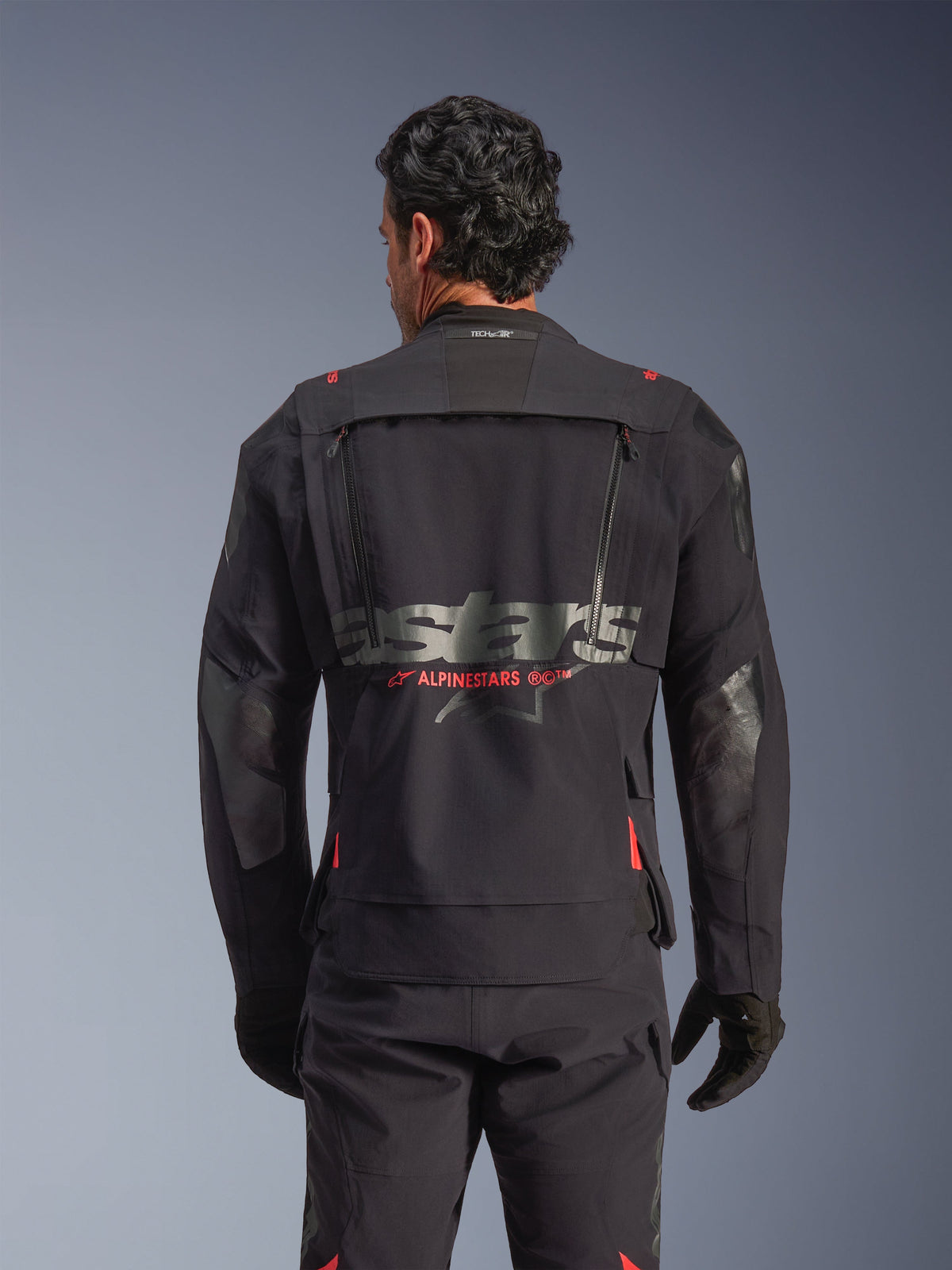 Alpinestars Halo Pro Drystar® XF Laminated Jacket in Black Dark Shadow, rear view on model, showing technical back ventilation panel with zippers, red Alpinestars logo accents, and Tech-Air® branding on the neck, modular adventure riding gear.