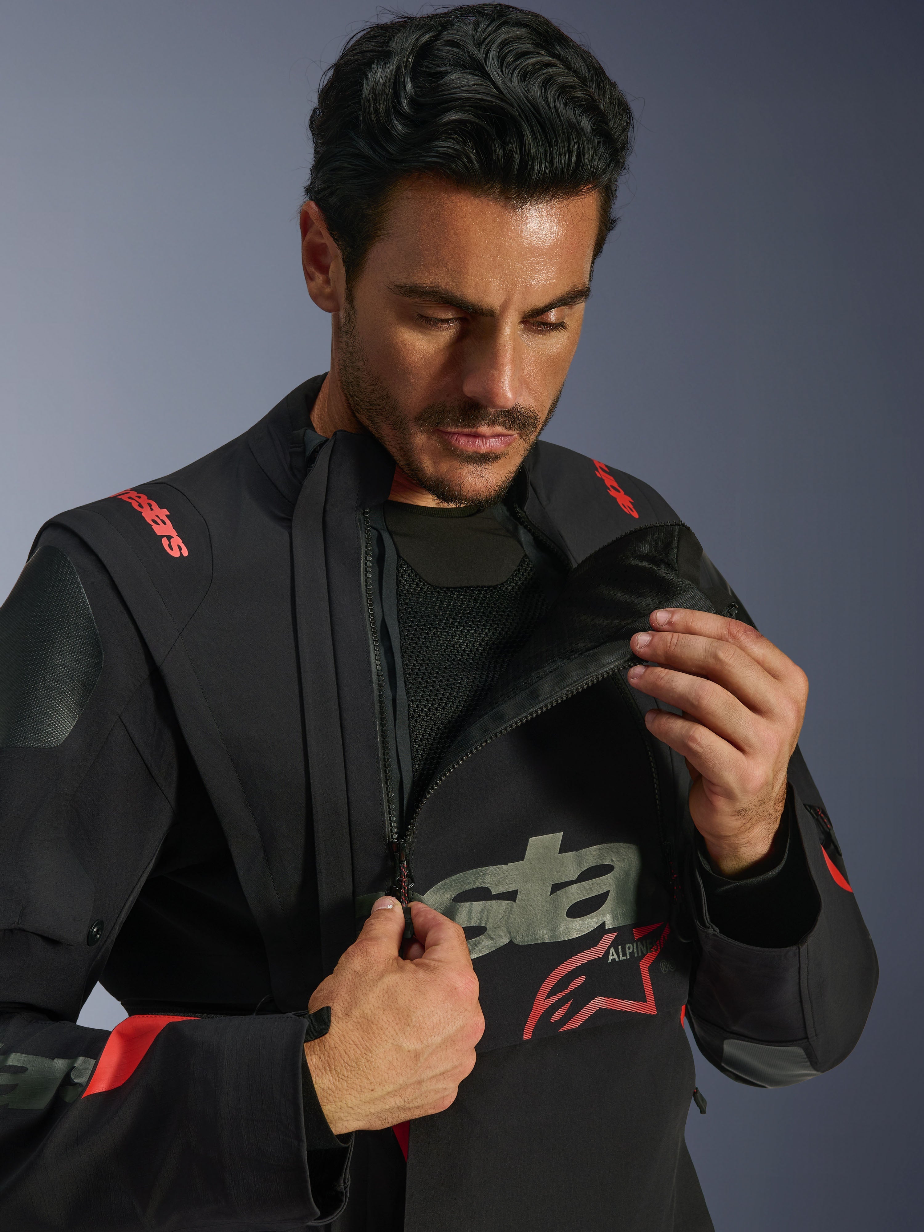 Casaco Alpinestars Halo Pro Drystar® XF Laminado, Black Dark Shadow, modelo a demonstrar o sistema de ventilação modular ao abrir o fecho do painel frontal assimétrico do peito, casaco de aventura touring com logótipo Alpinestars a vermelho e detalhes em malha técnica.