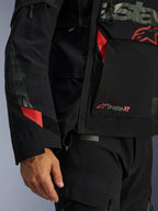 Casaco Alpinestars Halo Pro Drystar® XF Laminado, casaco de motociclismo, preto com detalhes vermelhos, grande plano destacando o logótipo Drystar® XF, textura técnica laminada e detalhes ajustáveis nas mangas para condução de aventura
