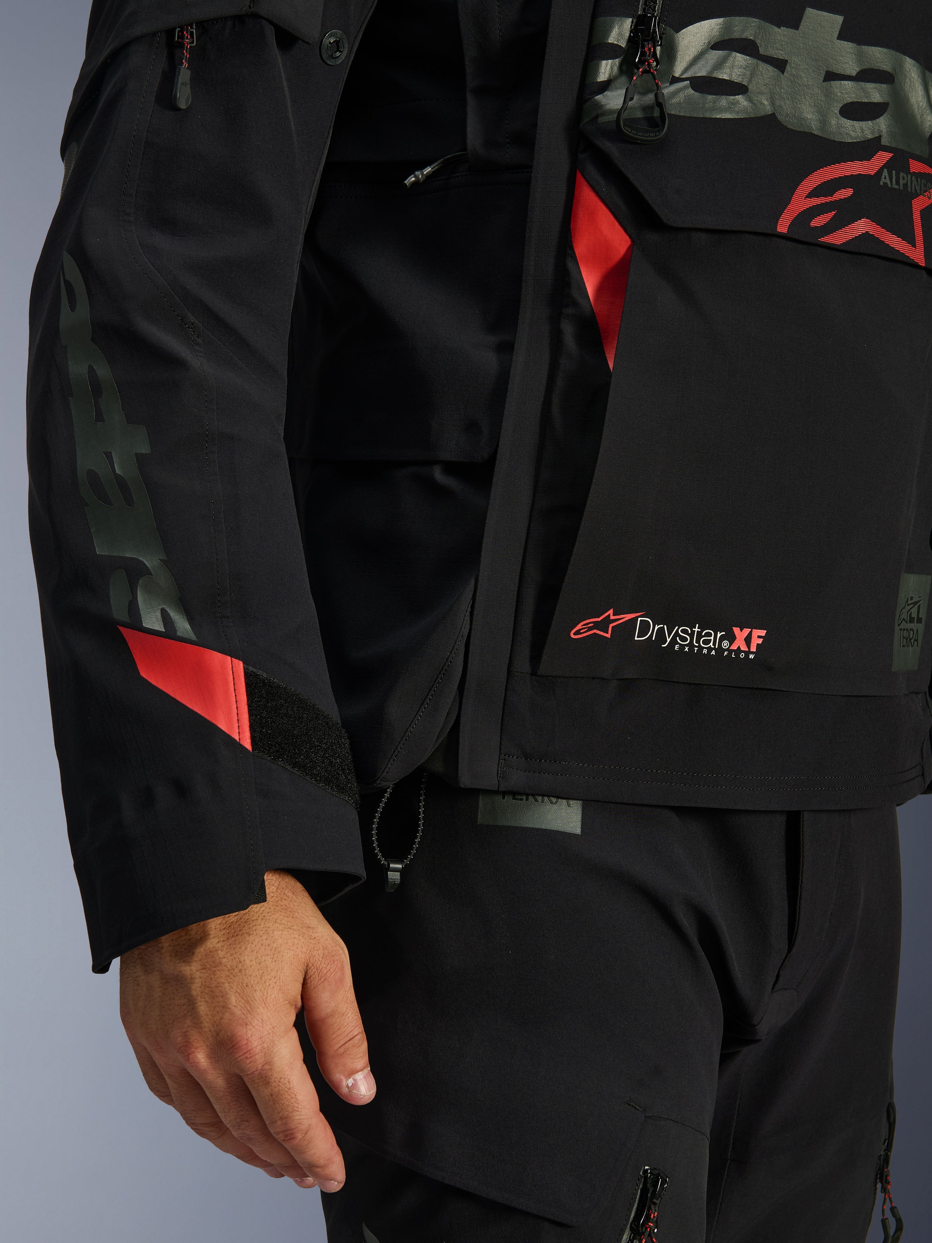 Casaco Alpinestars Halo Pro Drystar® XF Laminado, casaco de motociclismo, preto com detalhes vermelhos, grande plano destacando o logótipo Drystar® XF, textura técnica laminada e detalhes ajustáveis nas mangas para condução de aventura