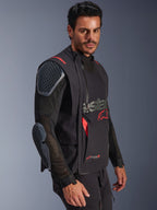 Alpinestars Halo Pro Drystar® XF Laminated Jacket, Preto e Dark Shadow, casaco de motociclismo de aventura usado por modelo, configuração modular com mangas de malha e proteções integradas nos ombros e cotovelos, detalhes do logótipo em vermelho e fechos técnicos impermeáveis.