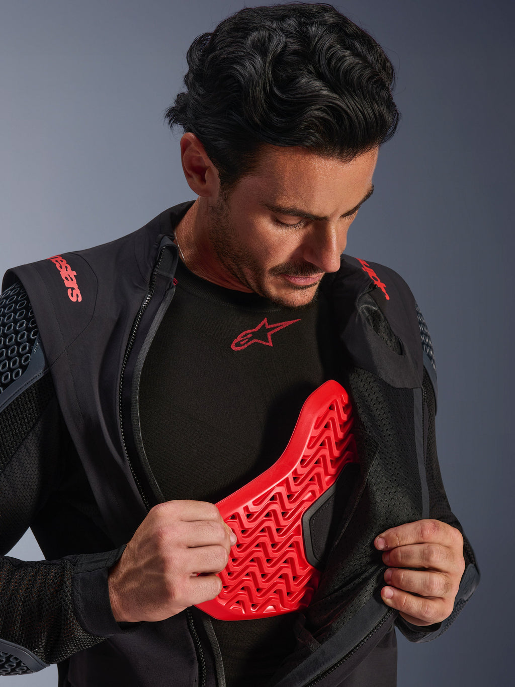 Casaco Laminado Alpinestars Halo Pro Drystar® XF em Black Dark Shadow, usado por um modelo e aberto para revelar um protetor de peito Nucleon Flex Pro vermelho, casaco técnico de motociclismo com armadura integrada, vestuário para condução de aventura.