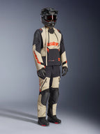 Alpinestars Halo Pro Drystar® XF Laminated Jacket em Mastic Black, casaco de motociclismo de aventura usado com calças a condizer, capacete integral, luvas e botas, apresentando painéis bege e pretos com logótipos vermelhos, design técnico multiestação