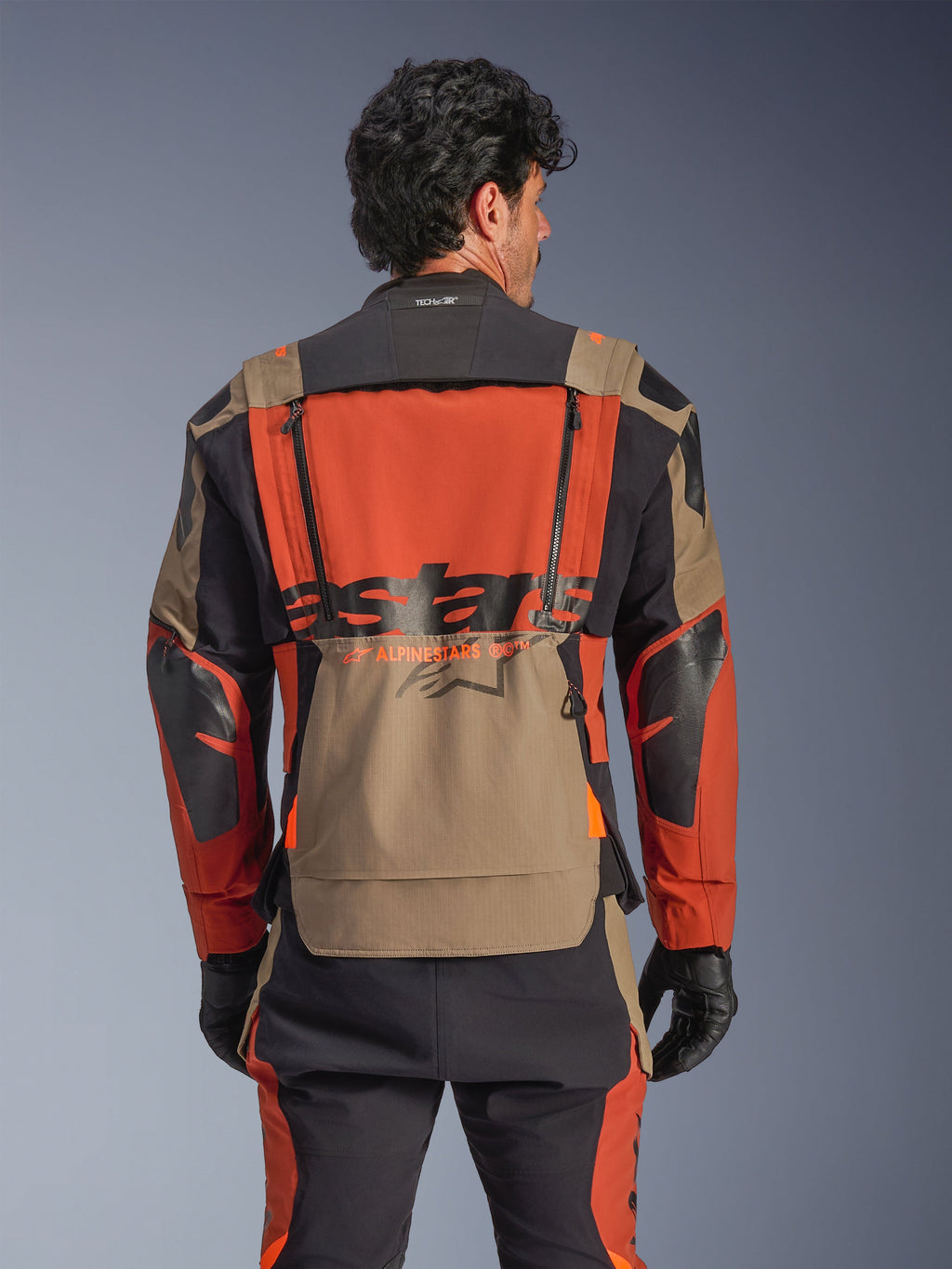 Casaco Laminado Alpinestars Halo Pro Drystar® XF, cor Walnut Rust Black, vista traseira, com um painel traseiro laranja grande com logótipo ASTARS em preto, bolso de armazenamento inferior em tom walnut e gola Tech-Air® Ready, usado com calças de aventura a condizer e luvas pretas