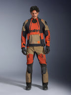 Modelo masculino a usar casaco laminado Alpinestars Halo Pro Drystar® XF e calças a condizer em Walnut Rust Black, equipamento modular de motociclismo de aventura com painéis de ventilação frontais e fechos, combinado com luvas e botas de motociclismo pretas.