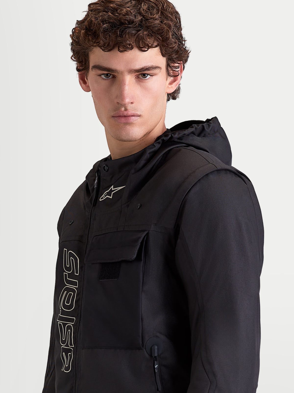 Alpinestars Morfex Parka Waterproof Jacket, casaco de moto urbano para homem em preto, retrato em plano aproximado de um modelo a vestir o casaco com capuz integrado e detalhes de bolso no peito