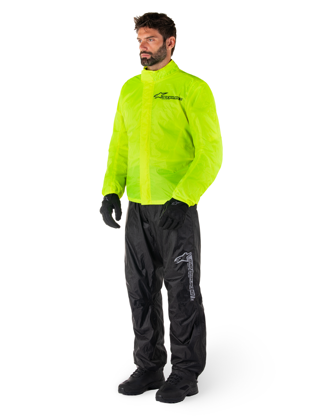 Man wearing Alpinestars Hurricane Rain V2 Jacket in Yellow Fluo and Hurricane Rain V2 Pants in Black, high-visibility waterproof motorcycle rain gear, featuring reflective logos on the chest and thigh, complete outfit with black gloves and boots.