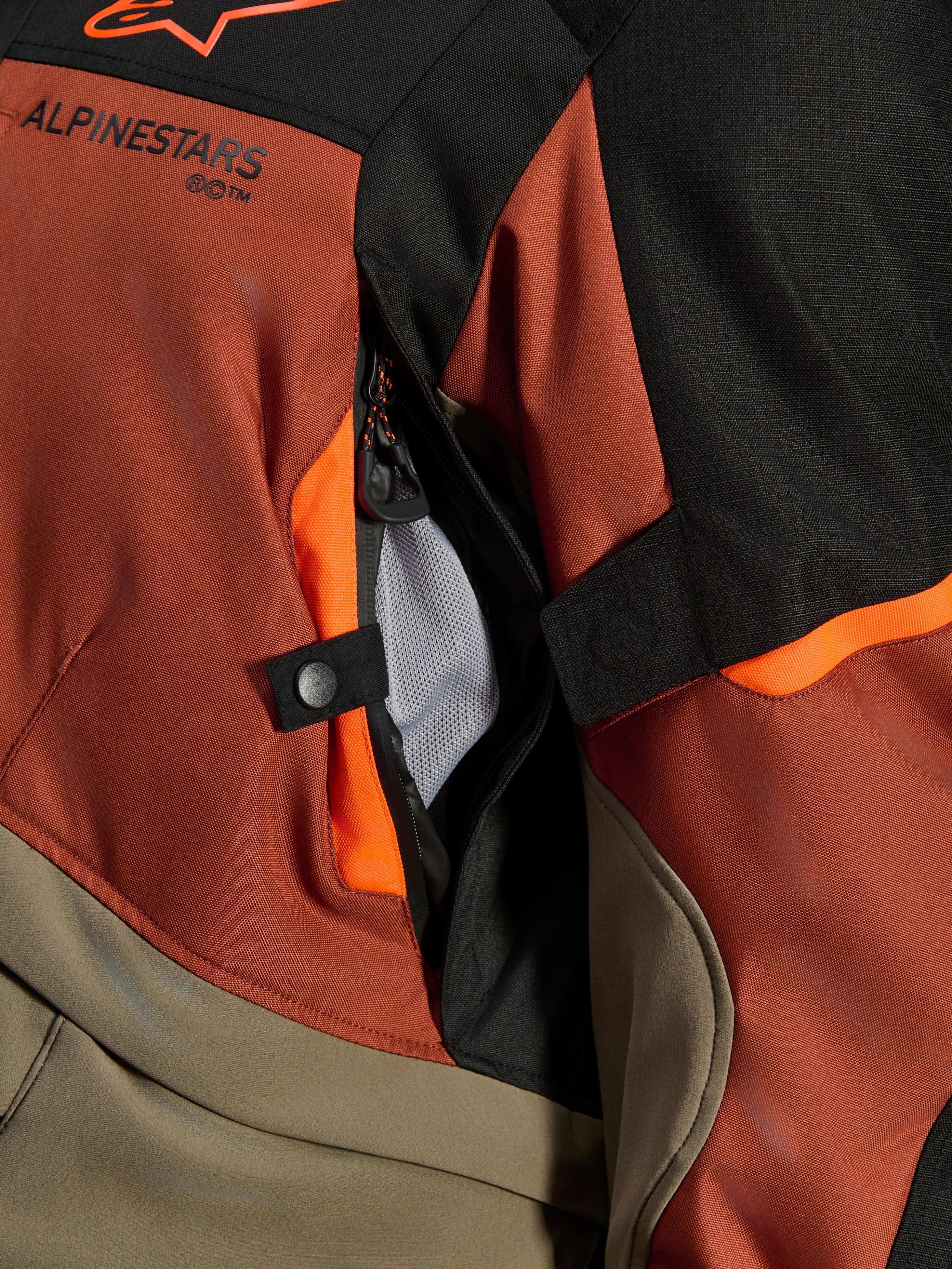 Casaco Alpinestars Andes V4 Drystar®, Walnut Rust Black, grande plano da abertura de ventilação direta com forro em malha, material têxtil durável com detalhes em laranja, botão de pressão e detalhe do logótipo Alpinestars.