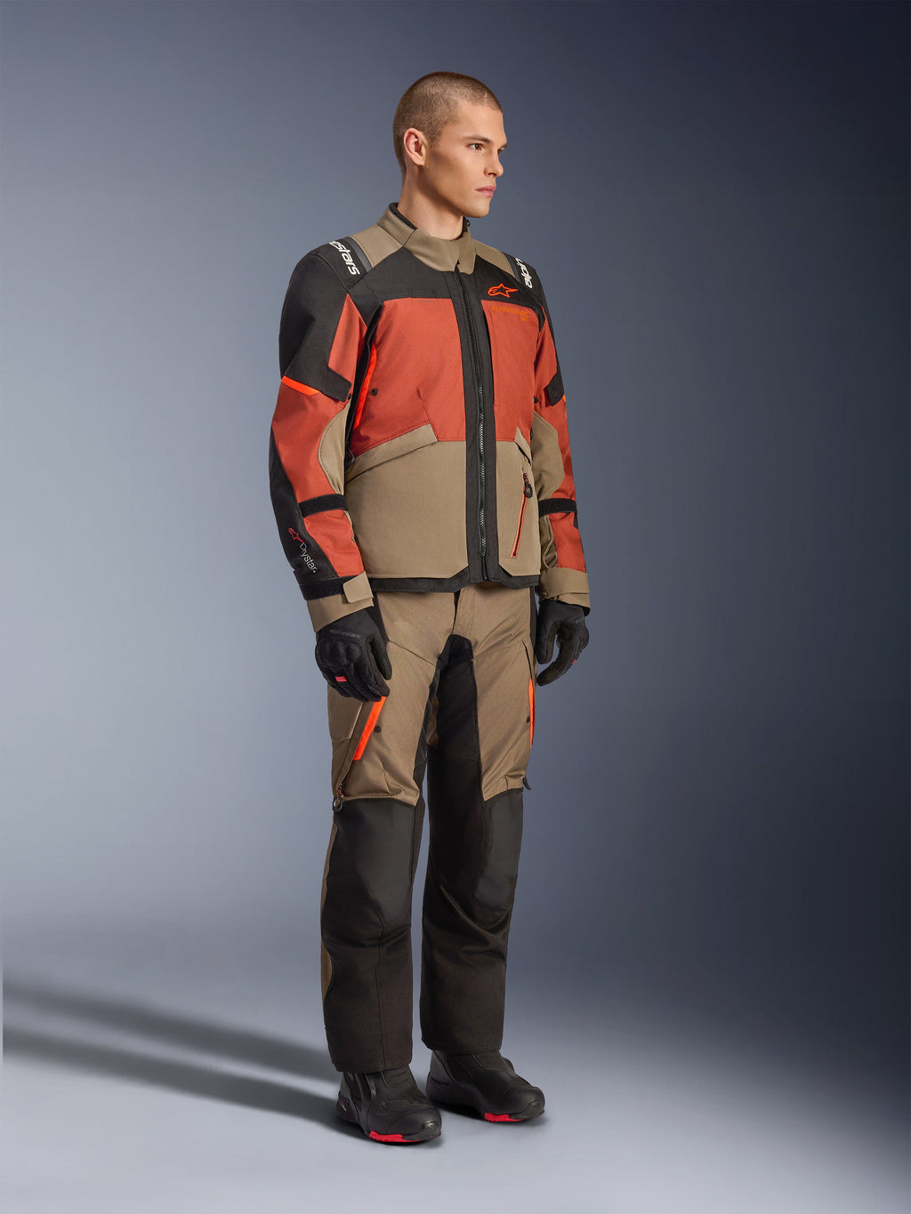 Casaco Alpinestars Andes V4 Drystar®, casaco de aventura e touring, Walnut Rust Black, usado com calças a condizer e botas pretas, com um design de blocos de cor em bege, ferrugem e preto, construção têxtil durável com fechos visíveis e logótipos da Alpinestars