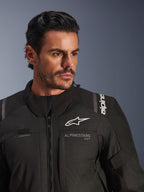 Casaco Alpinestars Andes V4 Drystar®, preto, vestido por um modelo masculino, plano aproximado que mostra o peito e os ombros, com logótipos Alpinestars brancos, material têxtil com detalhes de ventilação e laço para tubo de hidratação, equipamento de motociclismo adventure-touring