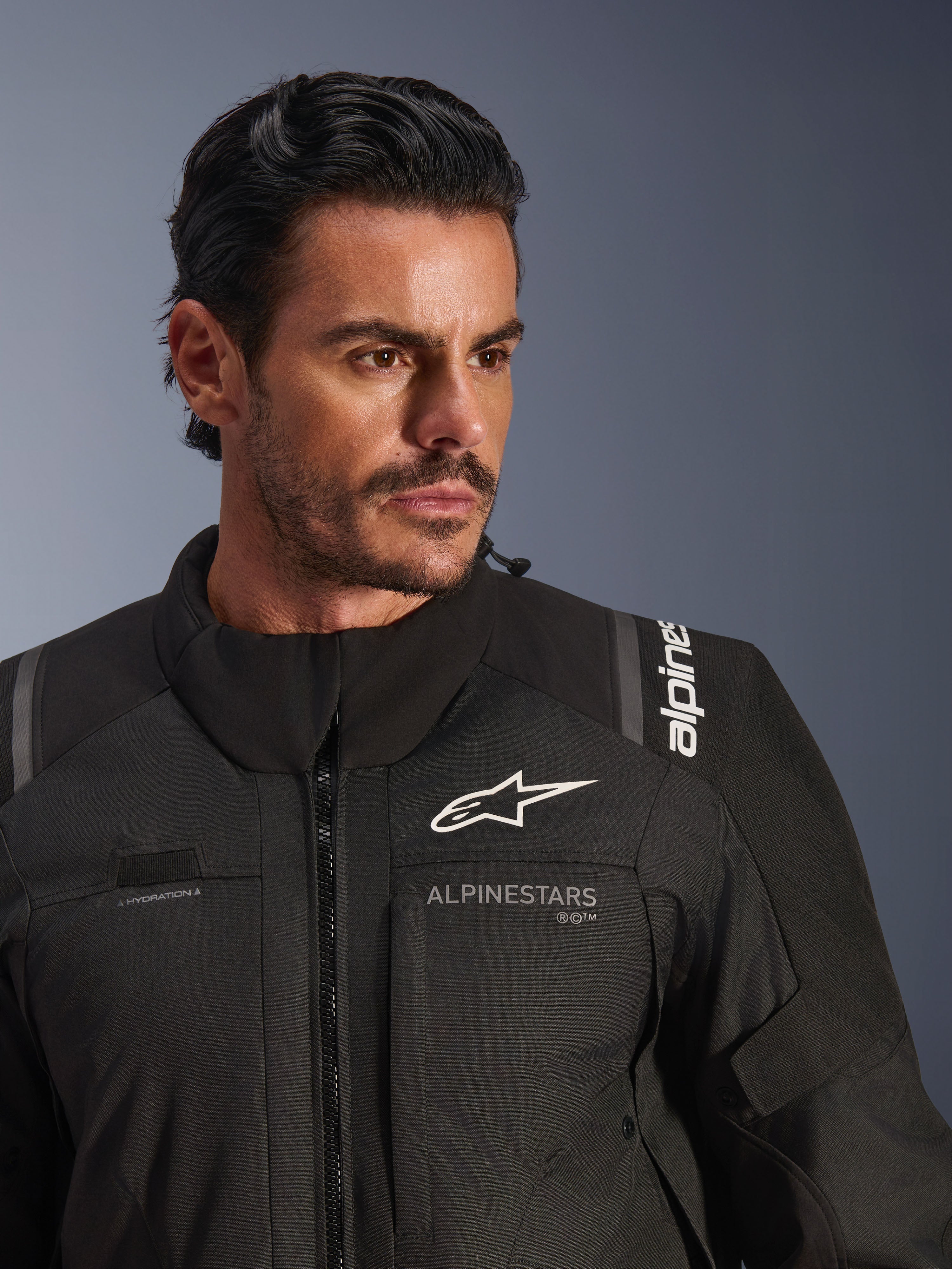 Casaco Alpinestars Andes V4 Drystar®, preto, vestido por um modelo masculino, plano aproximado que mostra o peito e os ombros, com logótipos Alpinestars brancos, material têxtil com detalhes de ventilação e laço para tubo de hidratação, equipamento de motociclismo adventure-touring