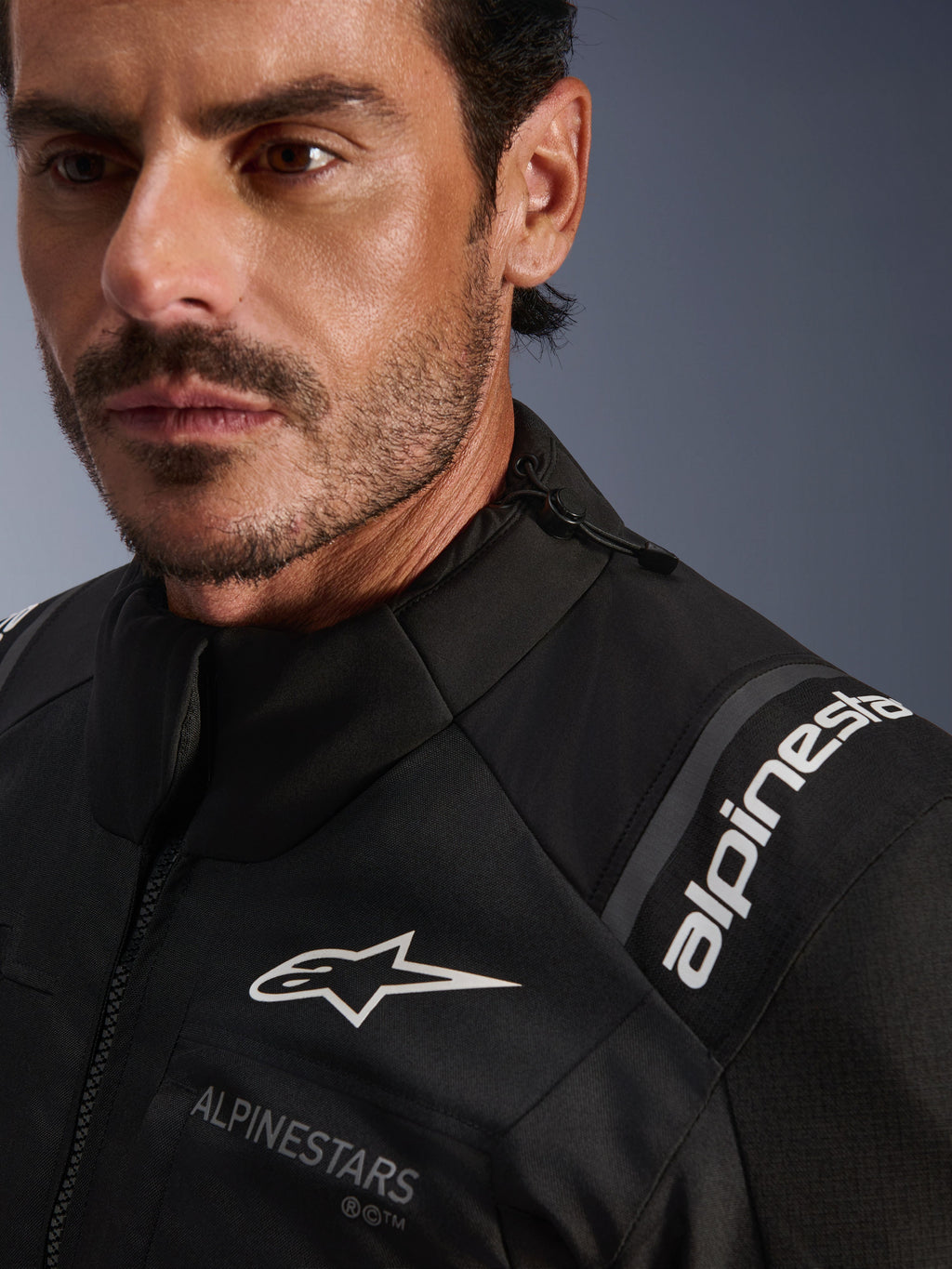 Alpinestars Andes V4 Drystar® Jacket, casaco de motociclismo em têxtil preto, pormenor em grande plano vestido por um homem, com logótipos Alpinestars brancos no peito e no ombro, cordão de ajuste na gola e design de aventura e turismo de alto desempenho.