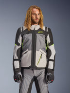 Casaco Alpinestars Andes V4 Drystar, casaco de moto para turismo de aventura, cinzento escuro e cinzento gelo com detalhes em amarelo néon, vestido por um modelo com calças e luvas a condizer, design têxtil multibolsos para condução em todas as condições climáticas
