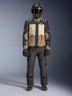 Casaco Alpinestars Andes V4 Drystar®, Walnut Mastic Black, casaco de motociclismo adventure touring com painéis bege e creme e detalhes laranja, usado por um motociclista com capacete de aventura preto, calças de motociclismo pretas e botas pretas, vista de corpo inteiro em estúdio