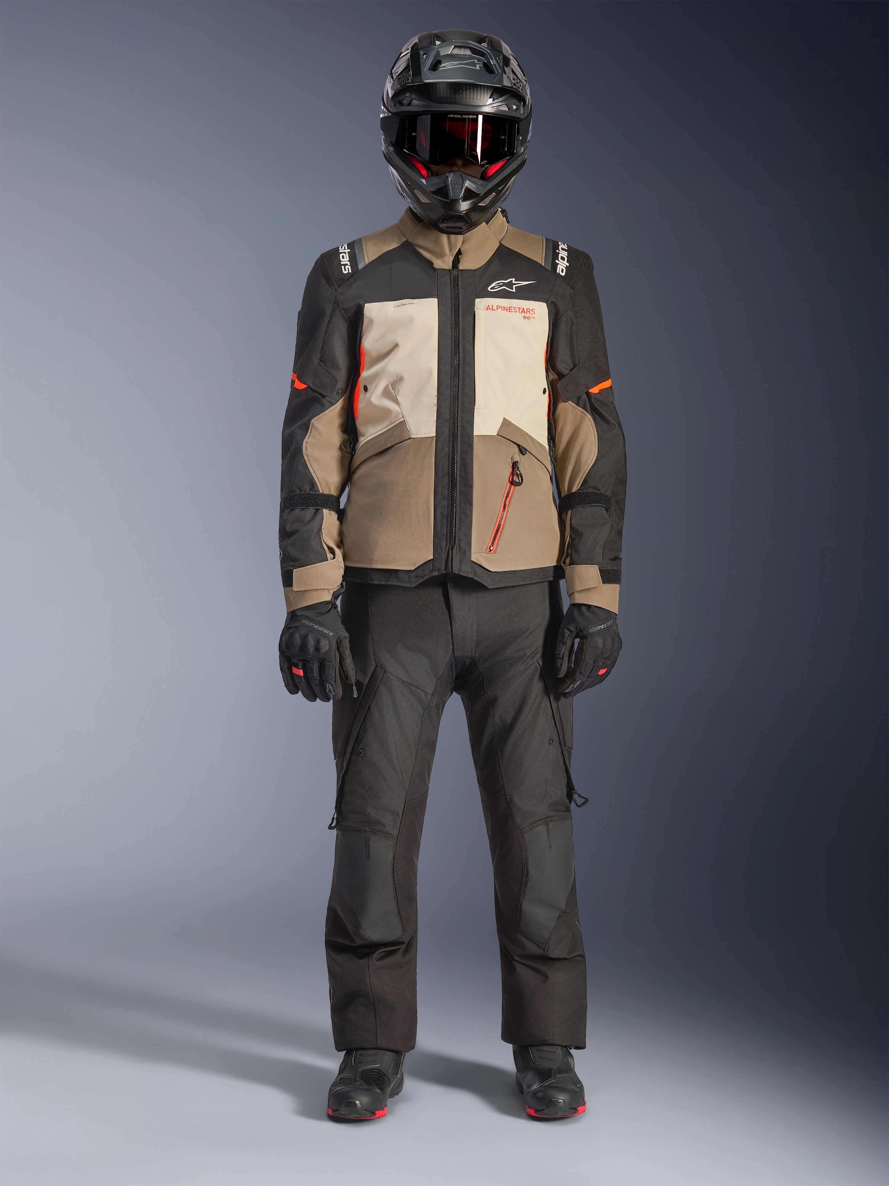 Casaco Alpinestars Andes V4 Drystar®, Walnut Mastic Black, casaco de motociclismo adventure touring com painéis bege e creme e detalhes laranja, usado por um motociclista com capacete de aventura preto, calças de motociclismo pretas e botas pretas, vista de corpo inteiro em estúdio