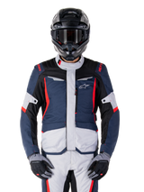Casaco Alpinestars ST-1 Waterproof, casaco touring de aventura, azul escuro, preto e vermelho vivo, usado com capacete de aventura preto e luvas cinzentas, com painéis cinza claro e detalhes vermelhos nos ombros e fechos, design elegante com a marca Alpinestars no peito, equipamento impermeável durável para motociclismo