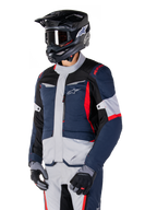 Alpinestars ST-1 Waterproof Jacket, adventure touring motorcycle jacket in Dark Blue, Black, and Bright Red, worn with a black helmet and grey gloves, featuring a modern design with functional pockets and Alpinestars branding.