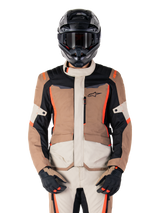 Alpinestars ST-1 Waterproof Jacket, casaco impermeável, Dark Khaki Sand Black Red Fluo, usado por um motociclista com capacete e luvas pretas, equipamento de aventura touring com painéis beges e castanhos e detalhes em vermelho fluorescente vibrante, vista frontal sobre fundo branco