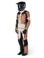 Casaco Impermeável Alpinestars ST-1, cáqui escuro, areia, preto e vermelho fluorescente, usado por um motociclista com equipamento completo de turismo de aventura com calças a condizer, capacete preto, óculos, luvas e botas, conjunto técnico de motociclismo para todas as condições climatéricas