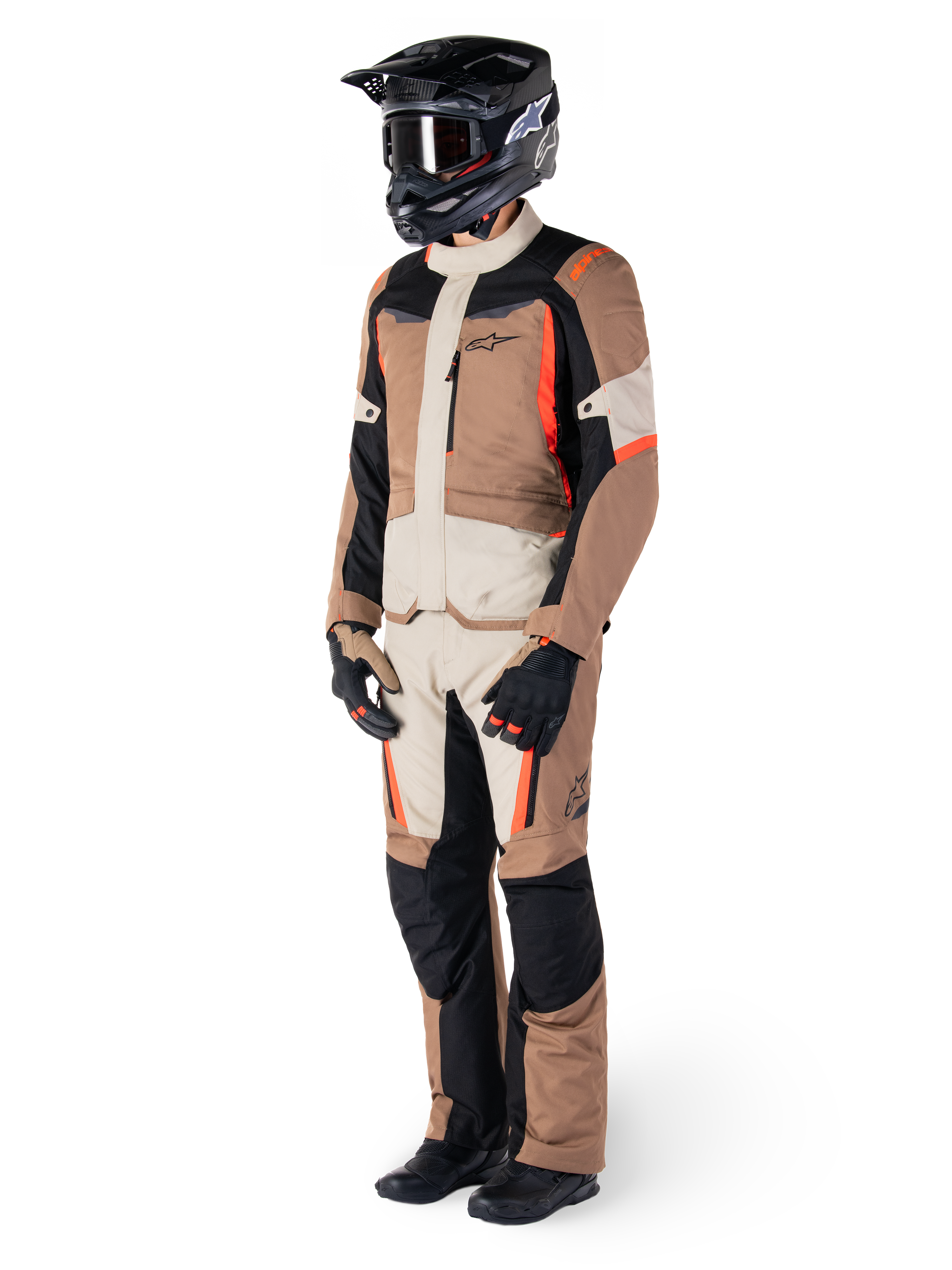 Casaco Impermeável Alpinestars ST-1, cáqui escuro, areia, preto e vermelho fluorescente, usado por um motociclista com equipamento completo de turismo de aventura com calças a condizer, capacete preto, óculos, luvas e botas, conjunto técnico de motociclismo para todas as condições climatéricas
