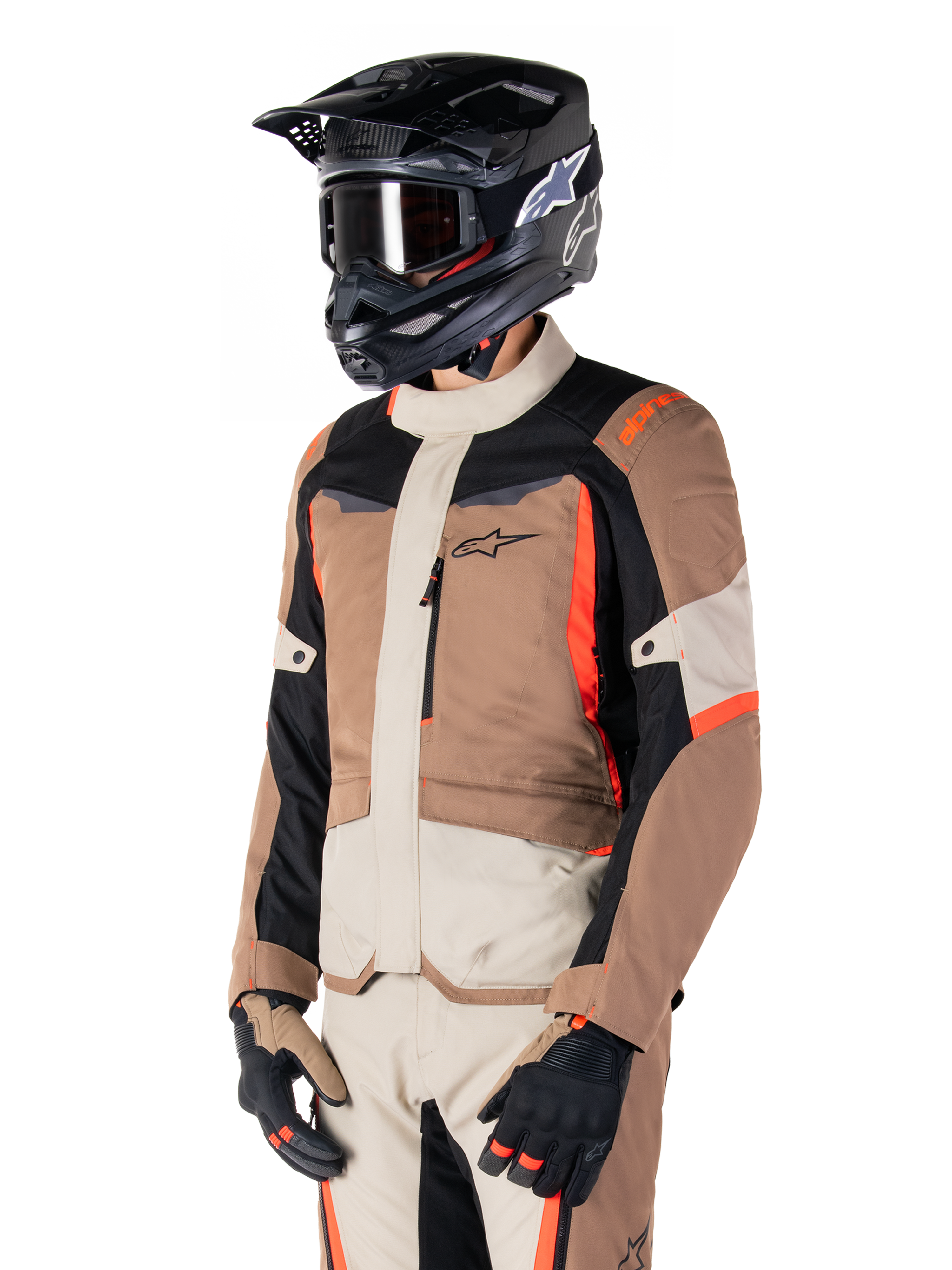 Casaco Alpinestars ST-1 Waterproof, casaco de touring de aventura, Dark Khaki Sand Black e Red Fluo, usado por um piloto com capacete de motocross preto e óculos de proteção, com design de vários painéis, bolsos cargo e logótipo Alpinestars no peito
