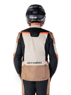 Casaco Alpinestars ST-1 Impermeável, Dark Khaki Sand Black Red Fluo, vista posterior, casaco de motociclismo de turismo de aventura com um grande painel traseiro cor de areia, mangas pretas e pormenores em vermelho fluorescente, mostrado num motociclista com um capacete preto.