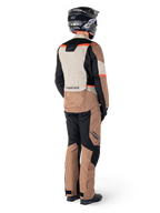 Casaco Impermeável Alpinestars ST-1, casaco de turismo de aventura, Dark Khaki Sand Black Red Fluo, vista traseira, usado com calças a condizer e capacete preto, com painéis em blocos de cores e detalhes em vermelho fluorescente.