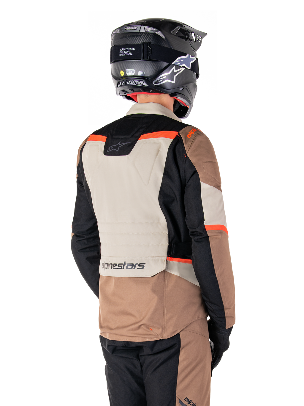 Casaco Impermeável Alpinestars ST-1, casaco de turismo de aventura, cáqui escuro, areia, preto e vermelho fluorescente, vista traseira com painéis têxteis em blocos de cor, detalhes em vermelho fluo e marca Alpinestars na zona inferior das costas, usado por um motociclista com capacete preto