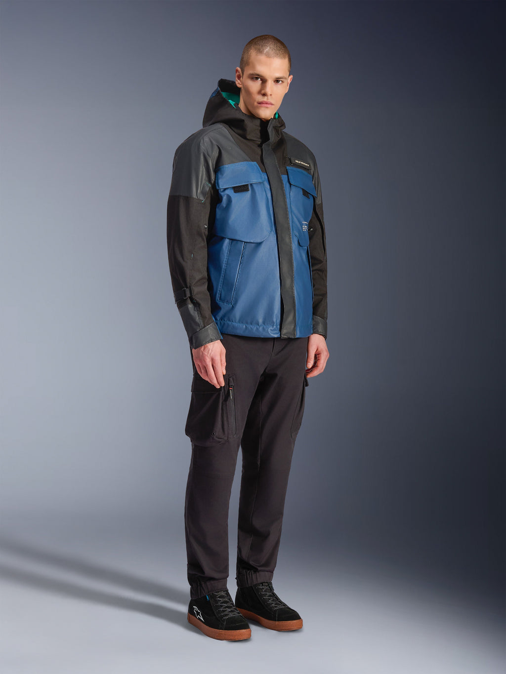Alpinestars Mospher Waterproof Jacket, Black and Dark Petrol Blue, worn with black cargo pants and black sneakers, urban commuter style with utility pockets and hood