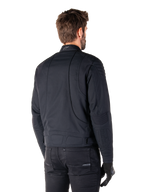 Casaco Alpinestars Clayton WR em preto, vista traseira de três quartos num modelo masculino, casaco de motociclista urbano com acolchoado nos ombros e cotovelos, linhas de costura técnicas e logótipo refletor na gola, combinado com calças e luvas pretas