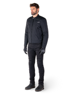 Motociclista a usar o Casaco Alpinestars Clayton WR, casaco de motociclista urbano preto, design de corte slim com pormenores acolchoados nos ombros e acabamento mate, combinado com calças técnicas de condução e luvas pretas.