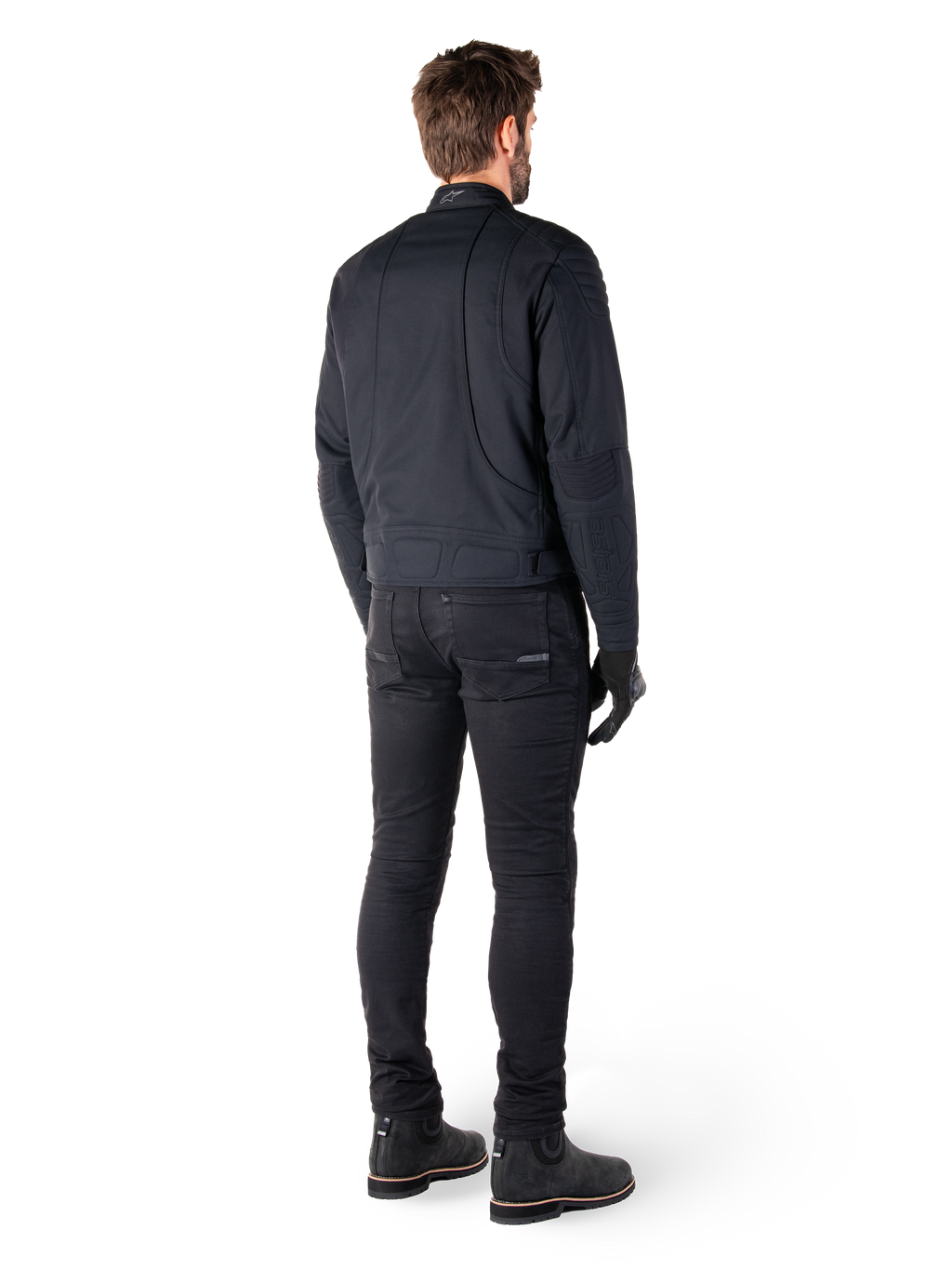 Vista traseira de um motociclista a usar o Casaco Alpinestars Clayton WR em preto, com painéis acolchoados nos cotovelos e ombros, costuras curvas ergonómicas e detalhes refletores na gola, combinado com calças e botas de motociclismo pretas para um visual urbano.