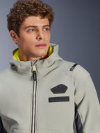 Alpinestars Moblast Waterproof Jacket, Iron Gray Dark Sage, close-up shot of male model wearing the jacket, featuring black Alpinestars logo and MO.ST.EQ. chest patches, bright yellow hood lining, and a modern technical design.