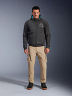 Casaco Impermeável Alpinestars Moblast, hoodie de motociclismo urbano preto com forro interior do capuz em azul-petróleo, usado com calças cargo bege e botas de cano alto pretas, vestuário de condução contemporâneo para todas as estações
