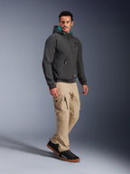 Modelo masculino a usar o Casaco Impermeável Alpinestars Moblast em preto, hoodie de motociclismo urbano com capuz forrado a azul-petróleo, combinado com calças cargo cáqui e ténis pretos, design minimalista moderno com tecido elástico técnico para deslocações em todas as condições meteorológicas