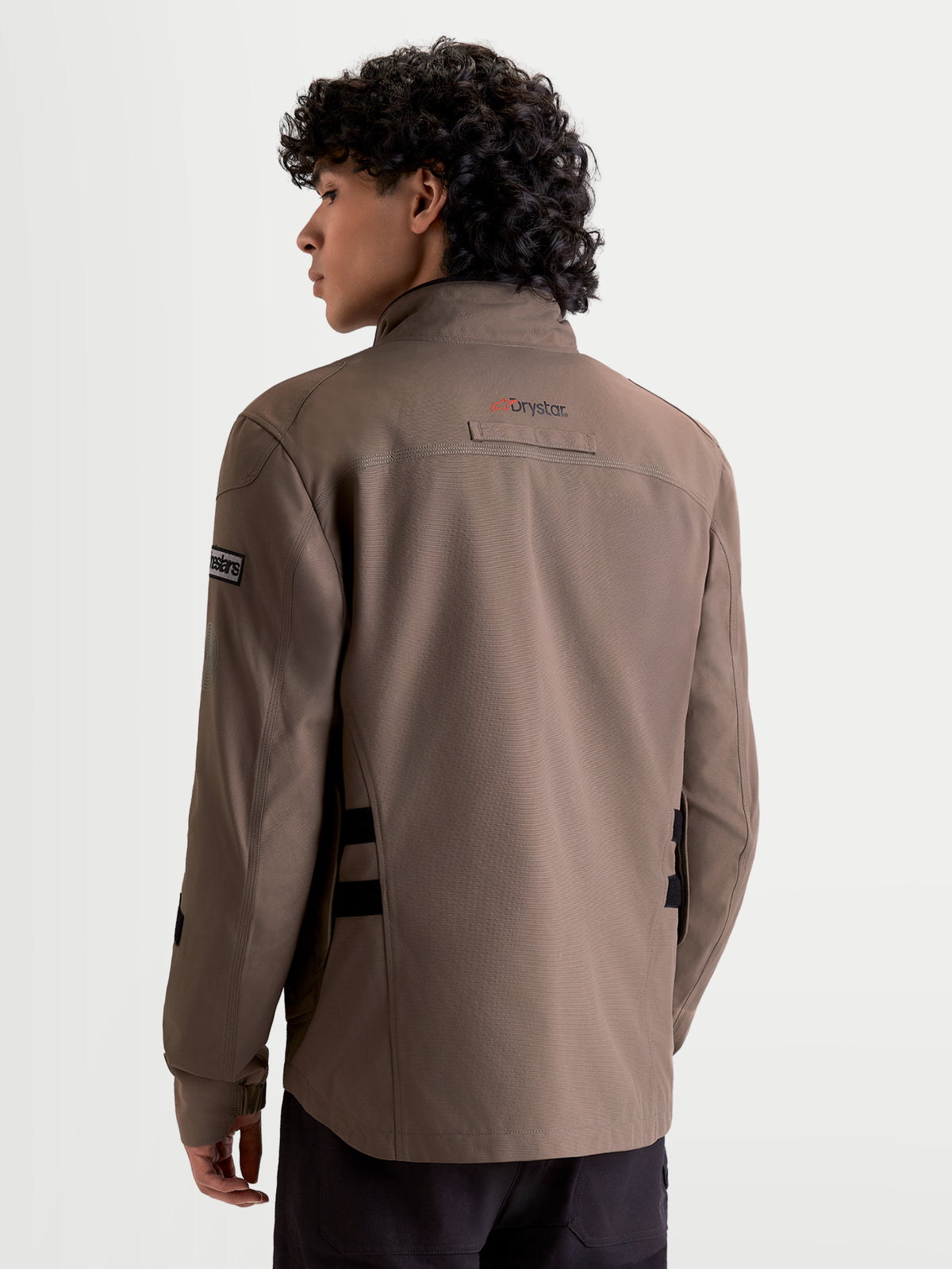 Altan Drystar Casaco da Alpinestars, casaco de moto urbano contemporâneo impermeável para homem em castanho e preto, vista traseira num modelo a mostrar a silhueta de estilo militar e o logótipo Drystar