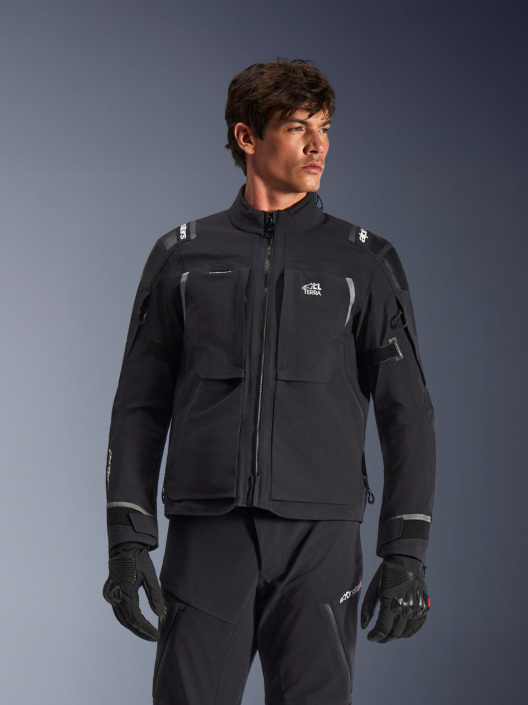 Alpinestars Andes Pro Drystar® XF Jacket, casaco de moto para turismo de aventura em preto e cinzento escuro, usado com calças e luvas a condizer, com construção técnica laminada, logótipo ALL TERRA no peito, detalhes refletores e punhos ajustáveis