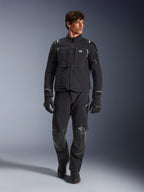 Modelo masculino a usar o Casaco Alpinestars Andes Pro Drystar® XF, casaco de motociclismo de aventura em preto e cinzento escuro, combinado com calças técnicas e luvas a condizer, com múltiplos bolsos e a marca 'Terra' no peito.