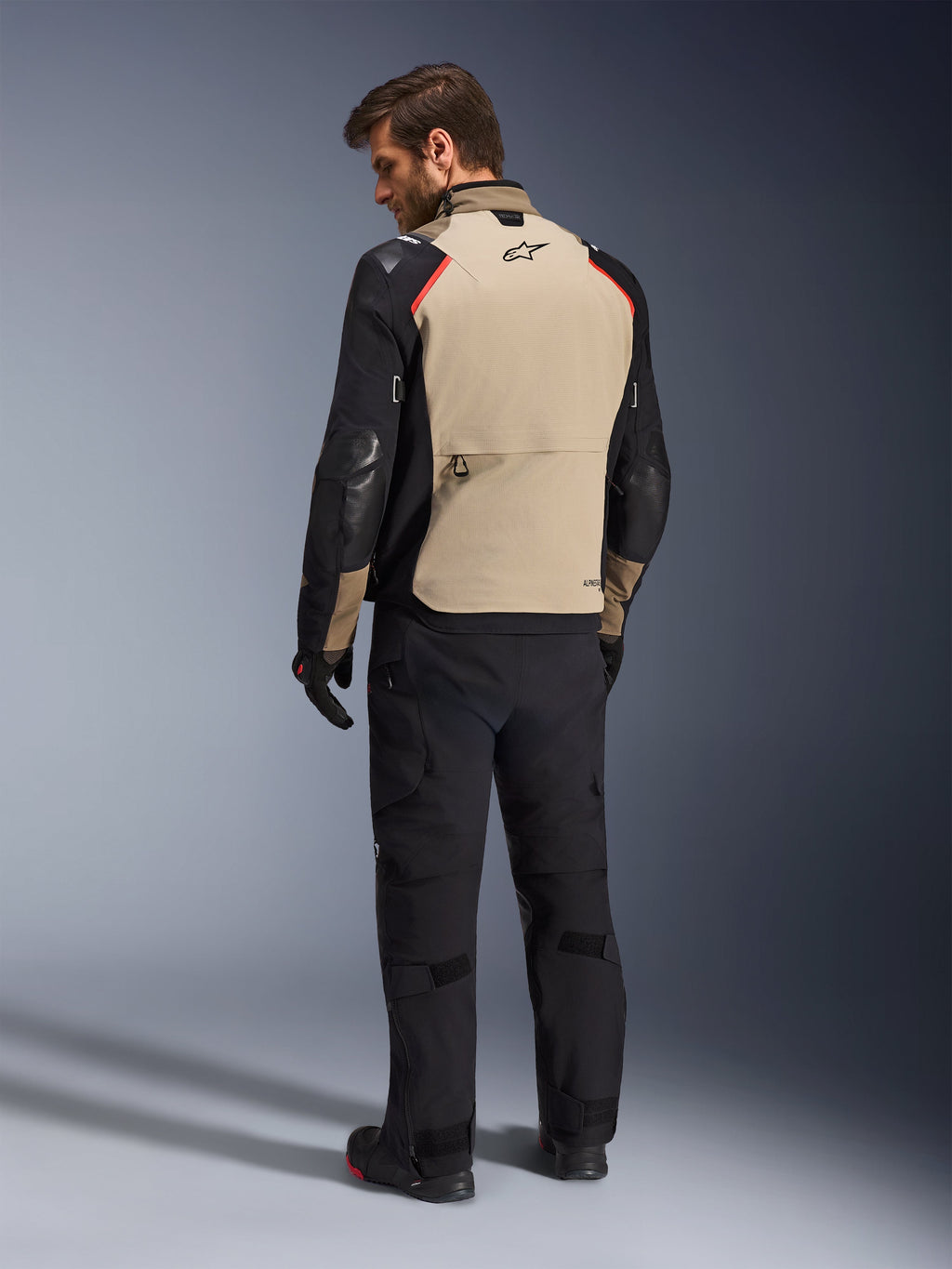 Casaco Alpinestars Andes Pro Drystar® XF, casaco de motociclismo, nogueira e preto com detalhes vermelhos, vista traseira no modelo, design de aventura touring com um grande bolso de arrumação traseiro, usado com calças e luvas de motociclismo pretas.