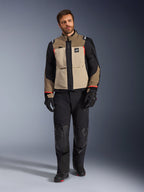 Modelo masculino a usar o casaco Alpinestars Andes Pro Drystar® XF em Walnut Aluminum, casaco de aventura e turismo bege e preto com detalhes em vermelho, combinado com calças, luvas e botas de motociclismo pretas, fotografia de corpo inteiro em estúdio de equipamento de proteção para condução.