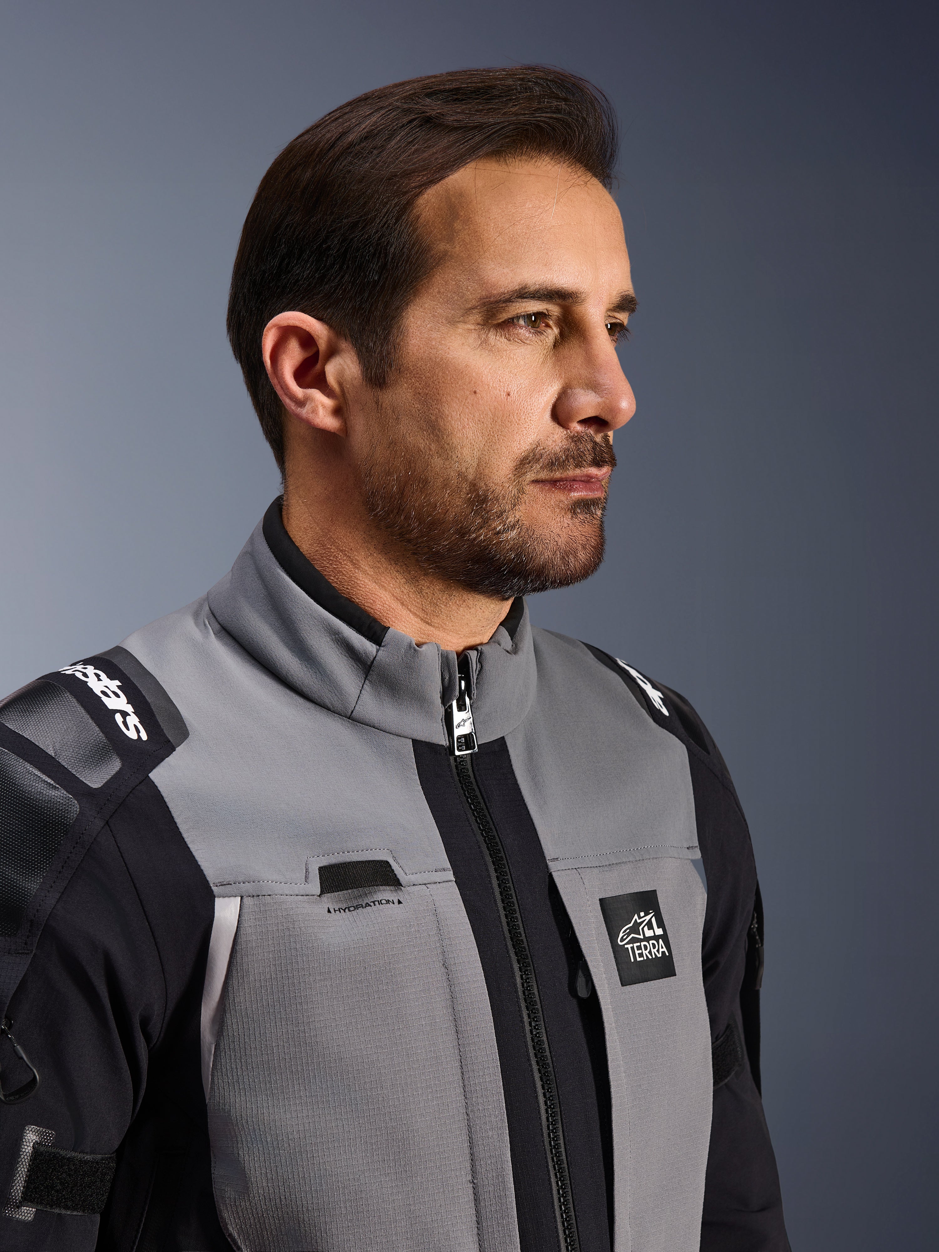 Alpinestars Andes Pro Drystar® XF Jacket, Motorcycle Adventure Jacket, Dark Gray and Black, close-up of the front torso and collar, featuring Terra branding and hydration routing detail, worn by a man in a studio setting