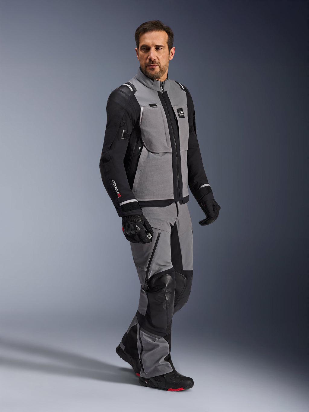 Alpinestars Andes Pro Drystar® XF Jacket, Adventure Motorcycle Jacket, Dark Gray and Black, worn by a model with matching textile pants and black gloves, featuring a multi-pocket design, technical 3-layer laminated shell, and articulated fit for long-distance adventure riding.