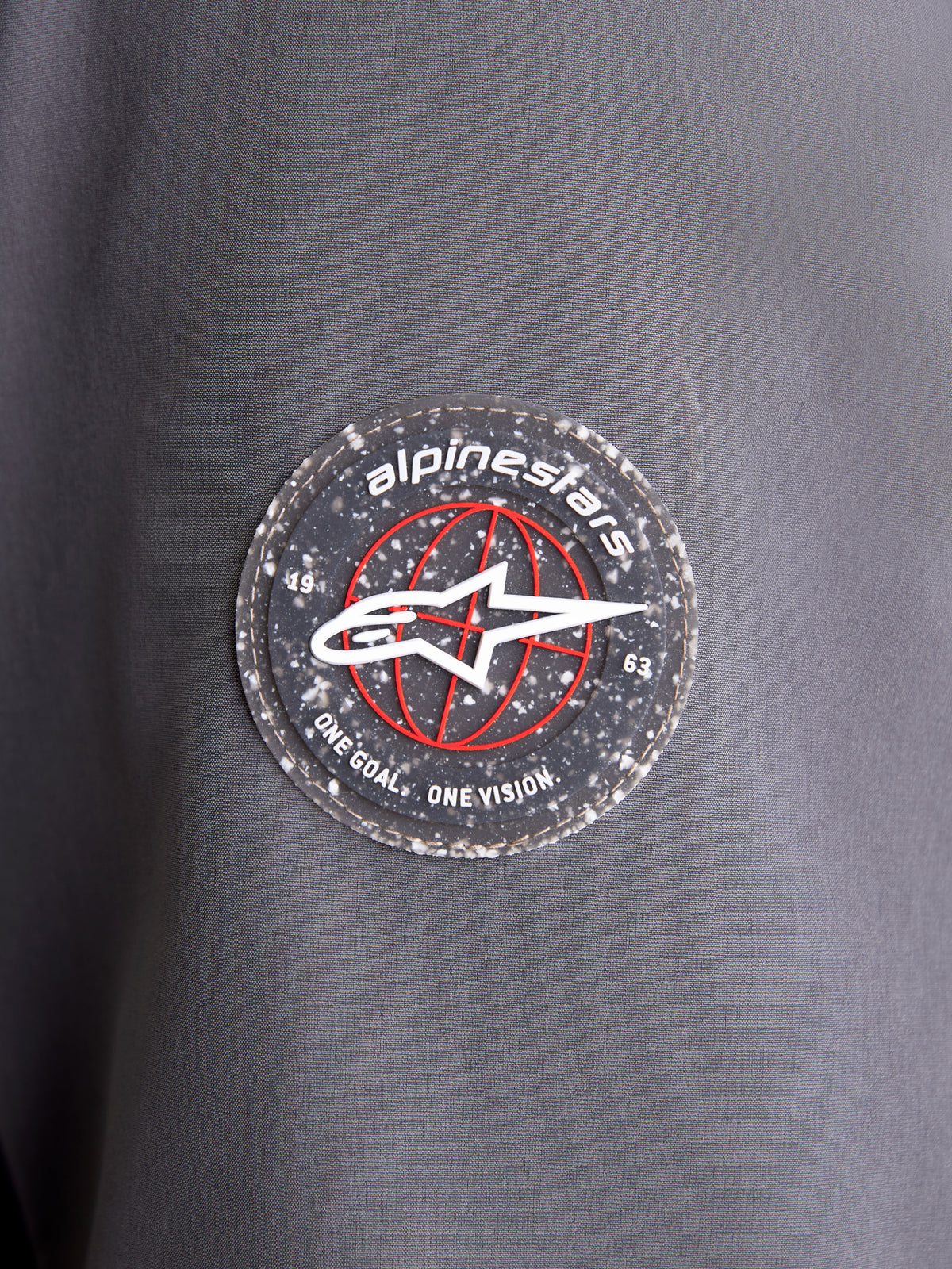 Alpinestars Therma-Tech WP Jacket, vista de pormenor do emblema circular com o logótipo da marca na manga em tecido cinzento escuro e preto, destacando o emblema A-star