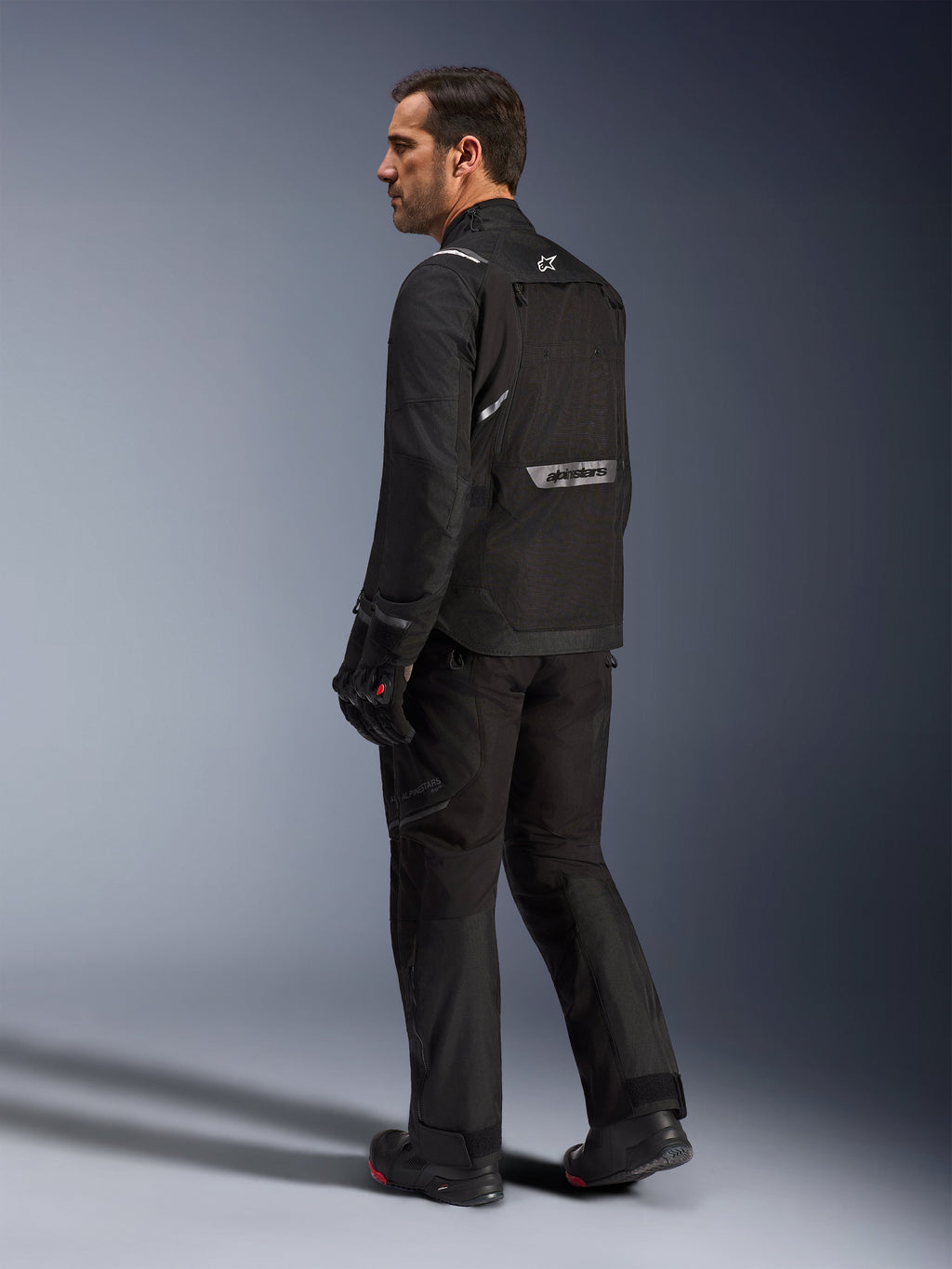 Alpinestars Cusco Drystar® Jacket, Black motorcycle jacket, back view of male model wearing full riding gear, featuring reflective branding on the back, textile construction with technical panels, coordinated outfit for road adventure touring