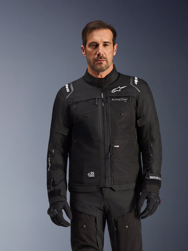 Alpinestars Cusco Drystar® Jacket, casaco de motociclismo preto, usado por um modelo com luvas e calças pretas a condizer, com construção em tecido técnico e logótipos Alpinestars brancos, concebido para turismo de aventura rodoviário