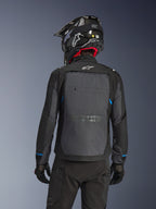 Piloto visto de costas a usar o Casaco Alpinestars Cusco Drystar® em preto e cinzento escuro, com um grande painel de ventilação cinzento nas costas e logótipo branco, combinado com um capacete de off-road preto e equipamento de condução preto para touring de aventura.